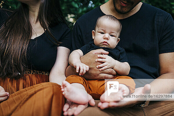 Cute baby boy sitting on father's lap by mother at park