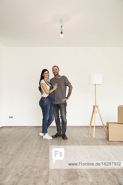 Lächelndes Paar mit elektrischer Lampe  das in einem neuen unmöblierten Haus an der Wand steht