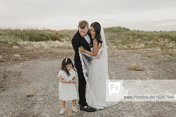 Eltern mit Tochter im Hochzeitskleid stehen gegen den Himmel