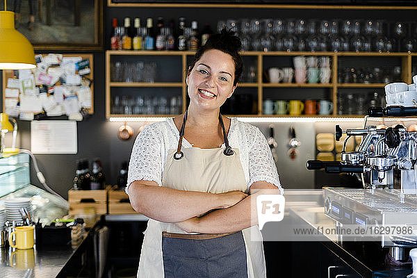 Lächelnde weibliche Barista mit verschränkten Armen in einem Café stehend