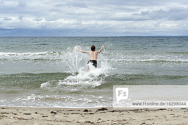 Hemdloser Junge genießt das Spritzen von Wasser am Strand
