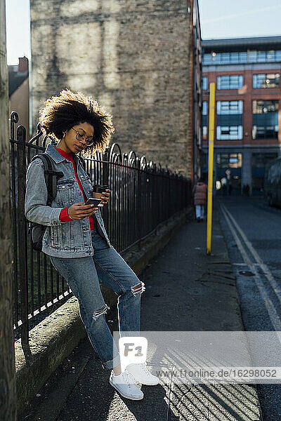 Junge Afro-Frau  die ein Mobiltelefon benutzt  während sie an einem Geländer auf einer Straße in der Stadt steht