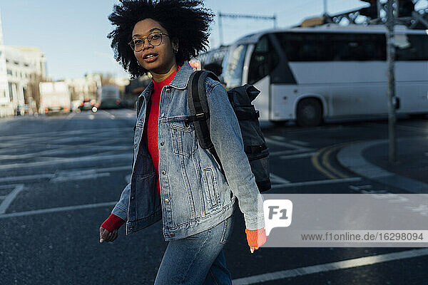 Afro junge Frau in Jeansjacke beim Überqueren der Straße in der Stadt