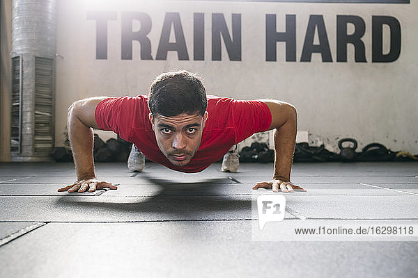 Selbstbewusster männlicher Sportler beim Üben von Liegestützen auf dem Boden im Fitnessstudio