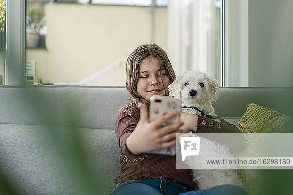 Mädchen nimmt Selfie durch Smartphone mit Hund auf Sofa