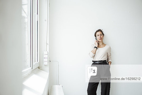 Selbstbewusste Unternehmerin im Gespräch über ein Smartphone  während sie an der Wand steht