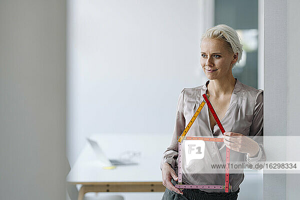 Nachdenkliche Geschäftsfrau  die ein Modell hält und an der Wand im Büro steht