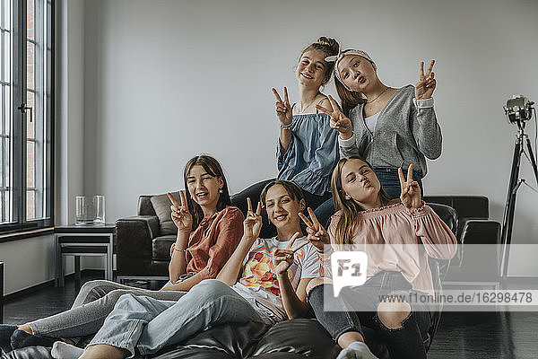 Smiling friends showing victory sign while sitting on sofa in loft apartment