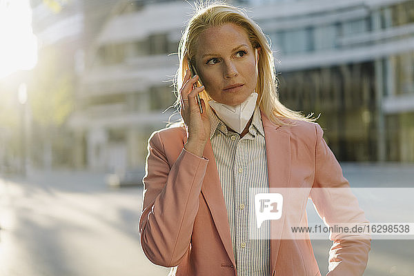 Female professional talking on mobile phone while looking away in city during COVID-19