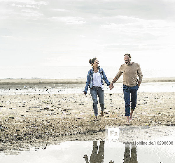 Glückliches Paar hält sich an den Händen  während es am Strand den Sonnenuntergang genießt