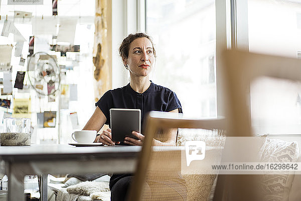 Nachdenkliche Besitzerin mit Kaffee auf dem Tisch und digitalem Tablet in einem Restaurant