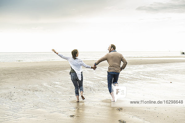 Cheerful couple holding hands while running at beach during sunset