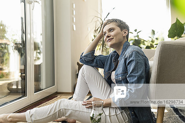 Nachdenkliche schöne Frau mit kurzen Haaren sitzt zu Hause im Sessel