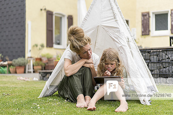 Verwirrte Mutter und Tochter schauen auf ein digitales Tablet  während sie am Wochenende im Zelt auf der Wiese sitzen