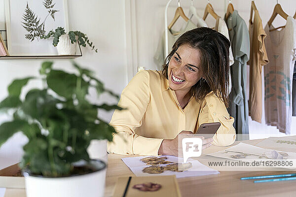 Lächelnde schöne junge Frau  die wegschaut  während sie mit ihrem Smartphone zu Hause sitzt