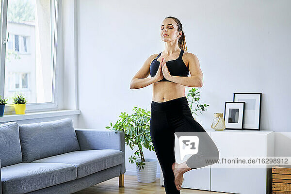 Woman practicing tree pose with eyes closed in living room