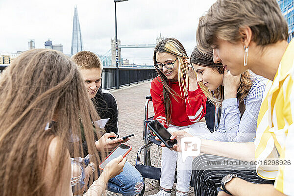 Male and female friends using mobile phones while spending leisure time together in city