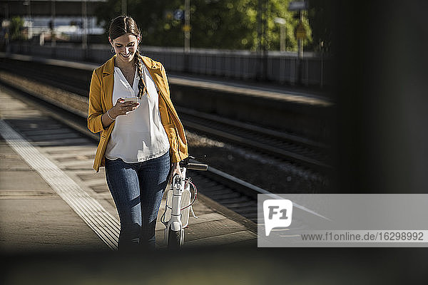 Junge Frau benutzt ihr Smartphone  während sie auf dem Bahnsteig spazieren geht