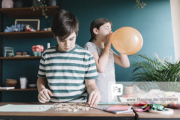 Junge spielt mit Buchstaben  während seine Schwester zu Hause einen Luftballon aufbläst