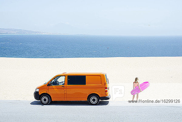 Weiblicher Reisender  der auf das Meer schaut  während er mit einem Surfbrett am Strand steht  an einem sonnigen Tag