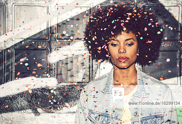 Confetti falling on thoughtful woman looking down while standing against wall