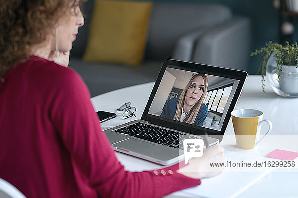 Young female entrepreneur is attending video conference through laptop at home office