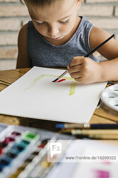 Cute boy holding paintbrush while painting on paper at home