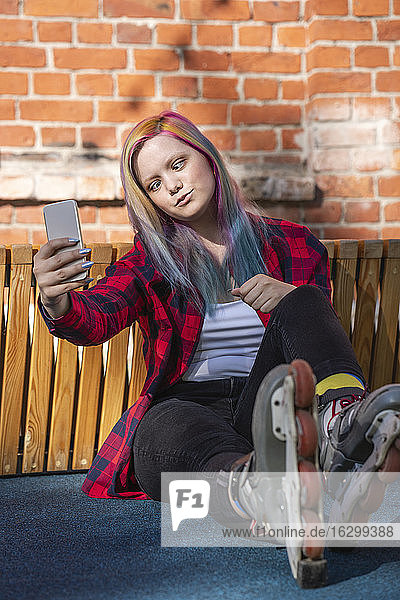 Junge Frau mit gefärbten Haaren und Rollschuhen  die ein Selfie mit ihrem Smartphone macht  mit schiefem Blick