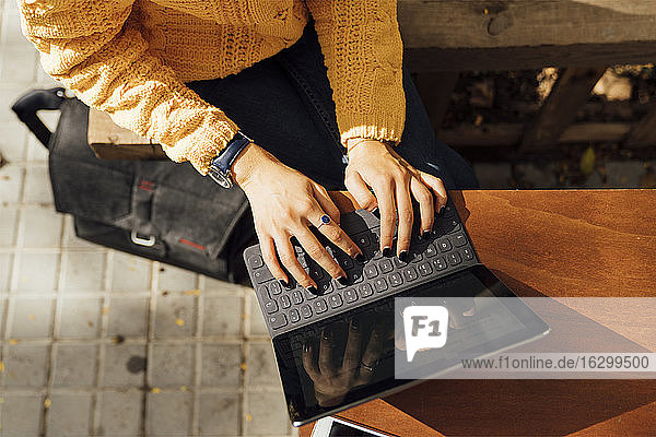 Mittelteil einer Studentin  die auf einer digitalen Tablet-Tastatur tippt  während sie in einem Straßencafé in der Stadt sitzt
