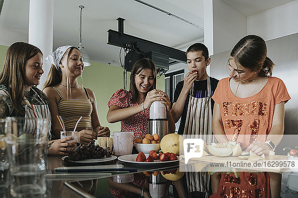 Eine Gruppe Jugendlicher steht in der Küche und bereitet Smoothies mit einem Mixer zu