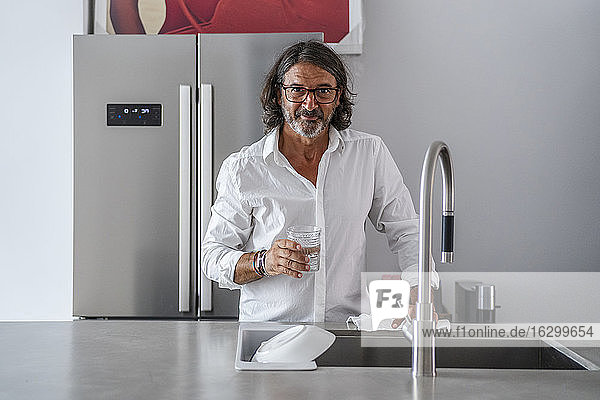 Lächelnder Mann  der Wasser trinkt  während er am Spülbecken in der Küche steht