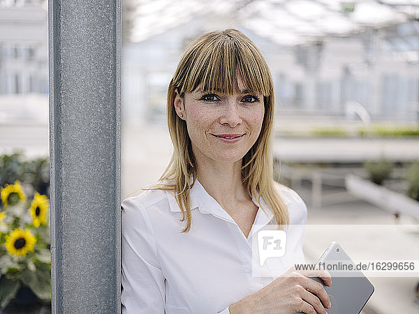 Close-up of smiling businesswoman with digital tablet standing in greenhouse