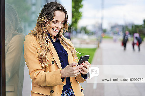 Glückliche Frau  die mit ihrem Smartphone SMS schreibt  während sie auf öffentliche Verkehrsmittel wartet