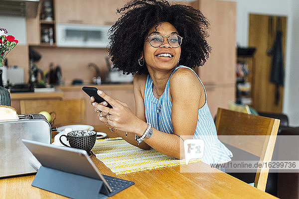 Junge Geschäftsfrau  die ein Mobiltelefon benutzt  während sie am Schreibtisch im Heimbüro sitzt