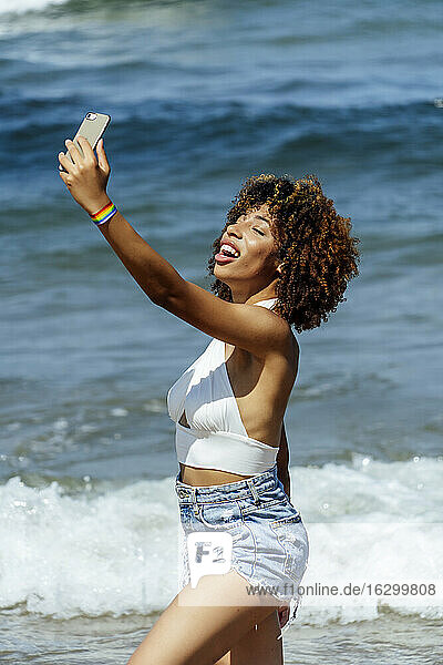 Junge Frau mit geschlossenen Augen  die ein Selfie macht  während sie an einem sonnigen Tag im Meer steht