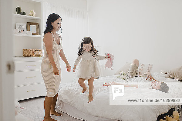 Smiling parents looking at daughter standing on bed at home