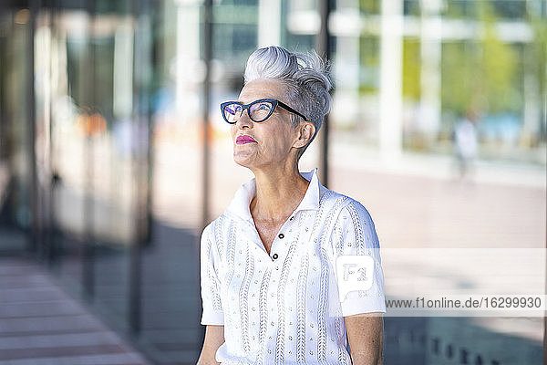 Smiling senior woman looking away while standing against glass window