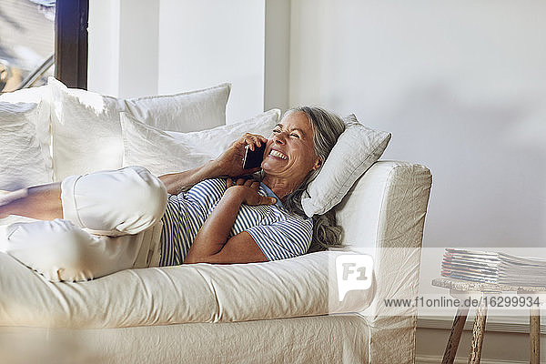 Cheerful woman talking on mobile phone over sofa in living room