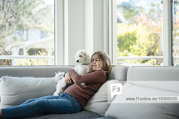 Nettes Mädchen umarmt Hund  während auf dem Sofa im Wohnzimmer sitzen