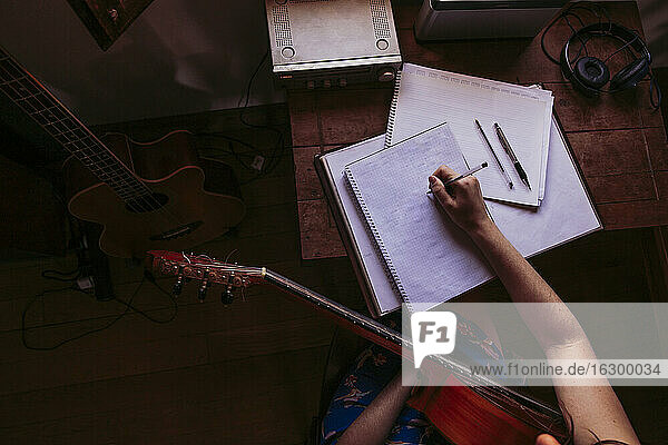 Junge Frau schreibt in ein Buch  während sie am Tisch Gitarre übt