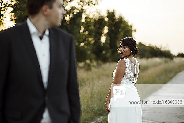 Junge Braut schaut Bräutigam an  während sie bei Sonnenuntergang auf dem Fußweg steht