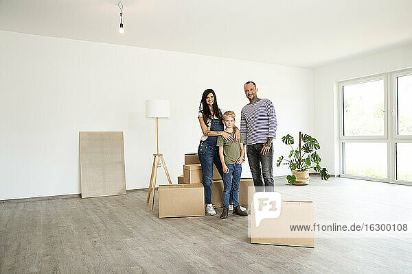 Happy family standing by cardboard boxes in new unfurnished home