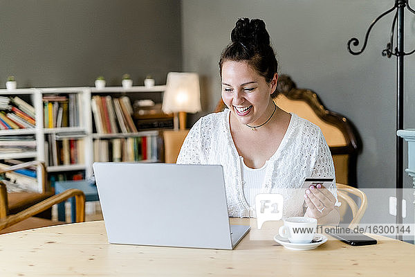 Glückliche  üppige junge Frau beim Online-Shopping am Laptop in einem Café