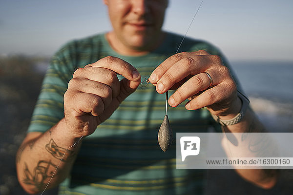 Close-up of mid adult man preparing fishing road at beach during sunset