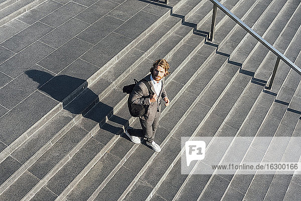 Männlicher Berufstätiger mit Tasche  der sich auf einer Treppe im Stadtzentrum an einem sonnigen Tag nach unten bewegt