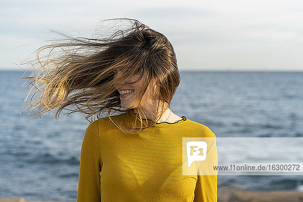 Glückliche Frau mit zerzaustem Haar  die sich am Meer erfreut