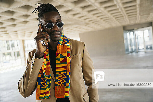 Fashionable man wearing traditional kenete talking on phone while standing in building