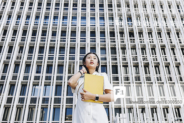 Female entrepreneur holding book while standing against financial district in city