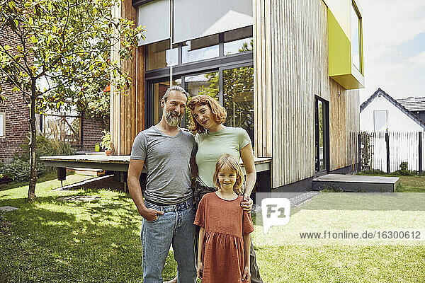 Smiling parents with daughter standing against tiny house in yard