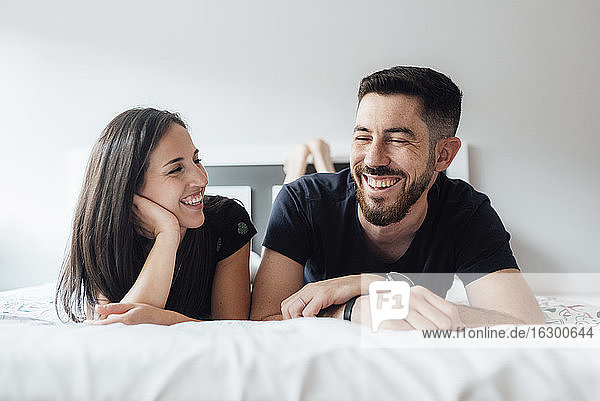 Romantic smiling couple lying on front in bedroom at home